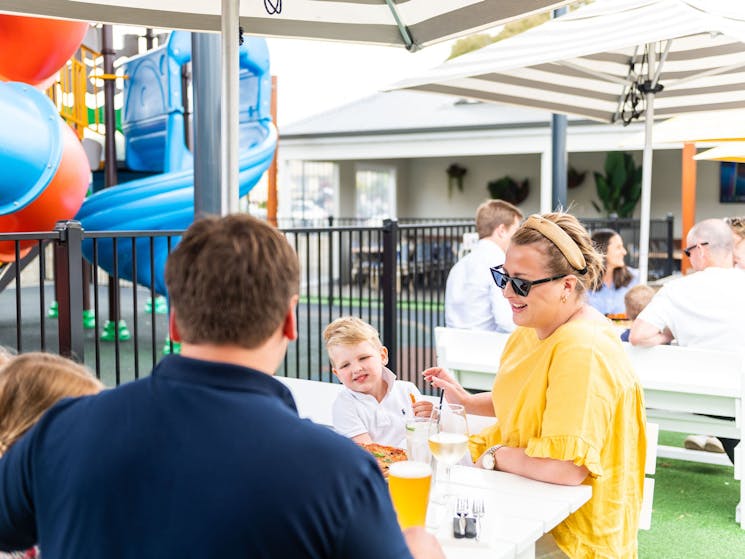 Man in vay shirt, Woman in yellow shirt and two children dining in sunny beer garden