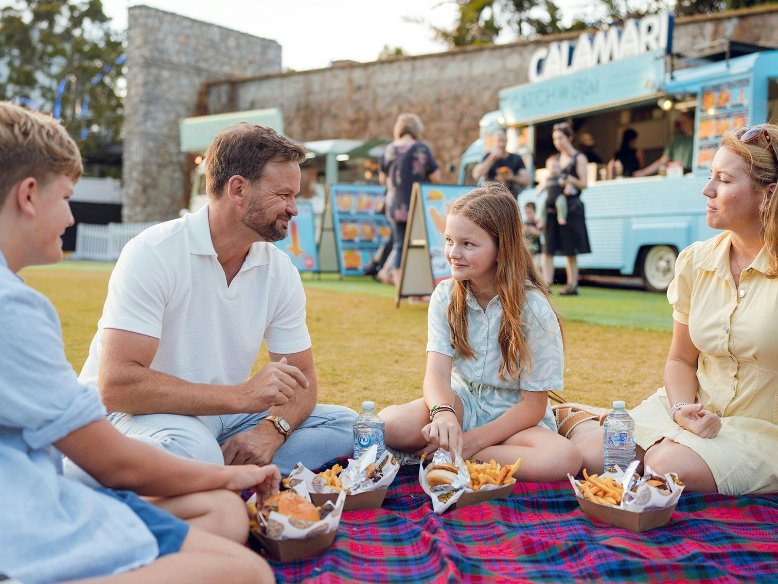 Family of four sat on a picnic rug on the grass enjoying food
