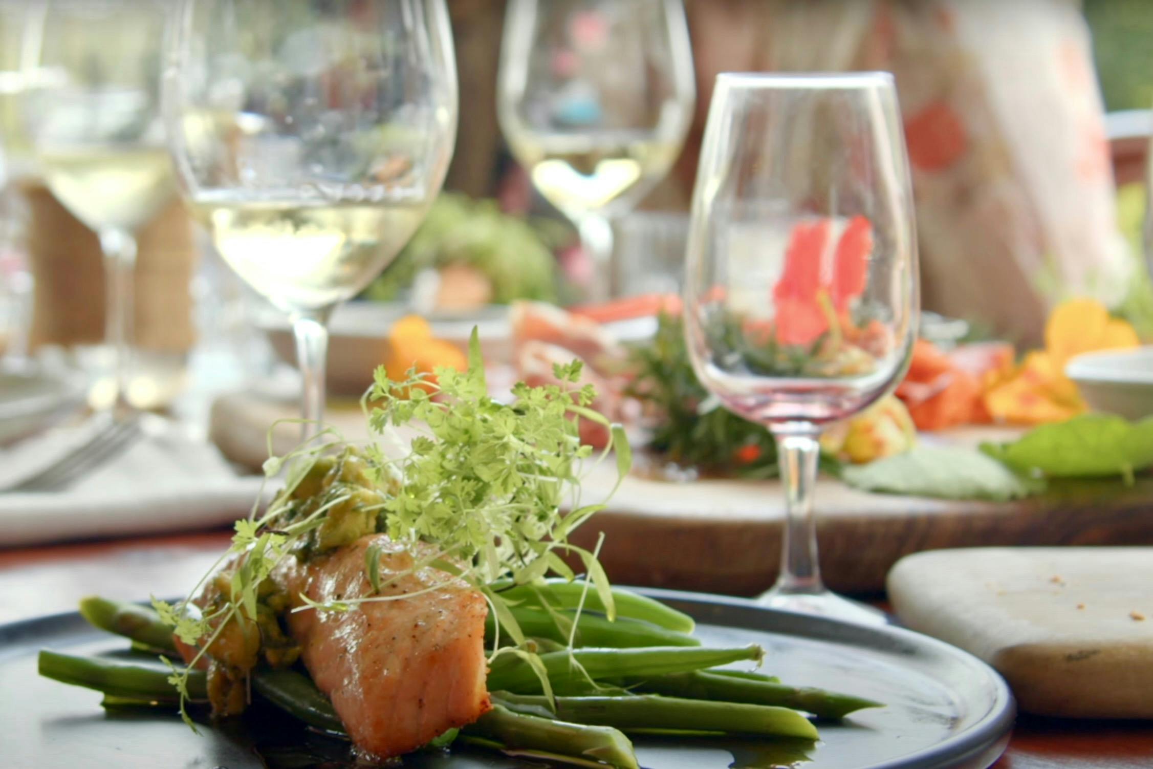 A plate of salmon with green beans and potatoes with glasses of wine in the background