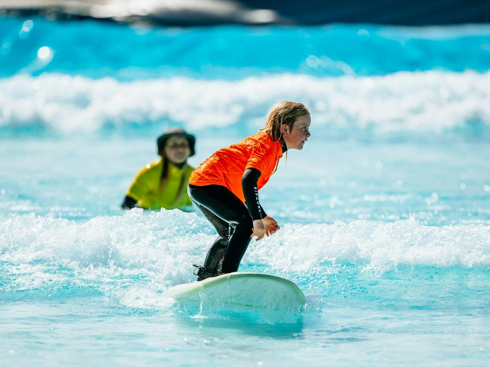 立ち上がる初心者サーファーを見つめるサーフコーチ