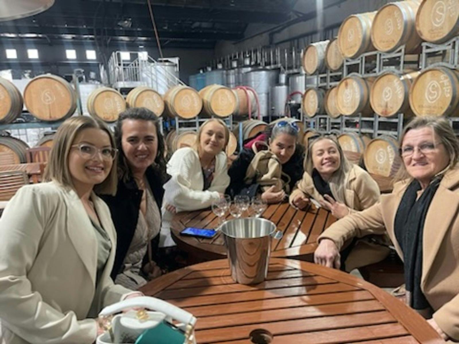 group having wine tasting with wine barrels in the background