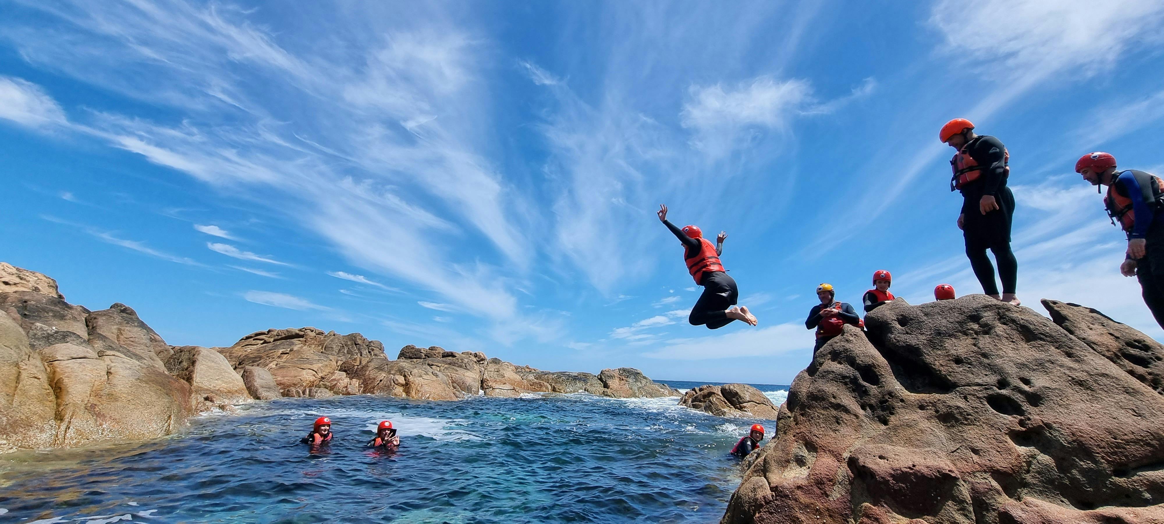 Hiker jumps into water from rocks wearing lifejacket and helmet while surrounding hikers watch