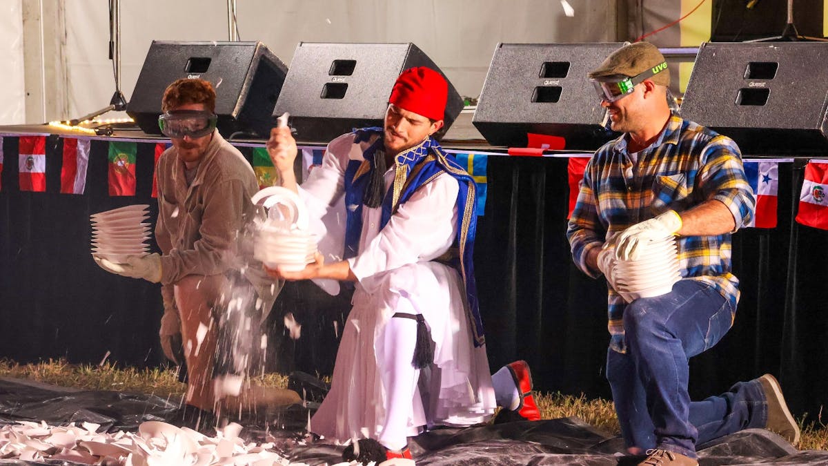Three men break stacks of plates on the ground during a cultural plate-smashing event.