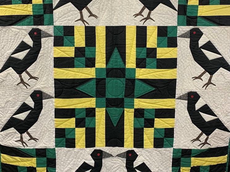 A quilt featuring a geometric design with a central green star with yellow and black with magpies