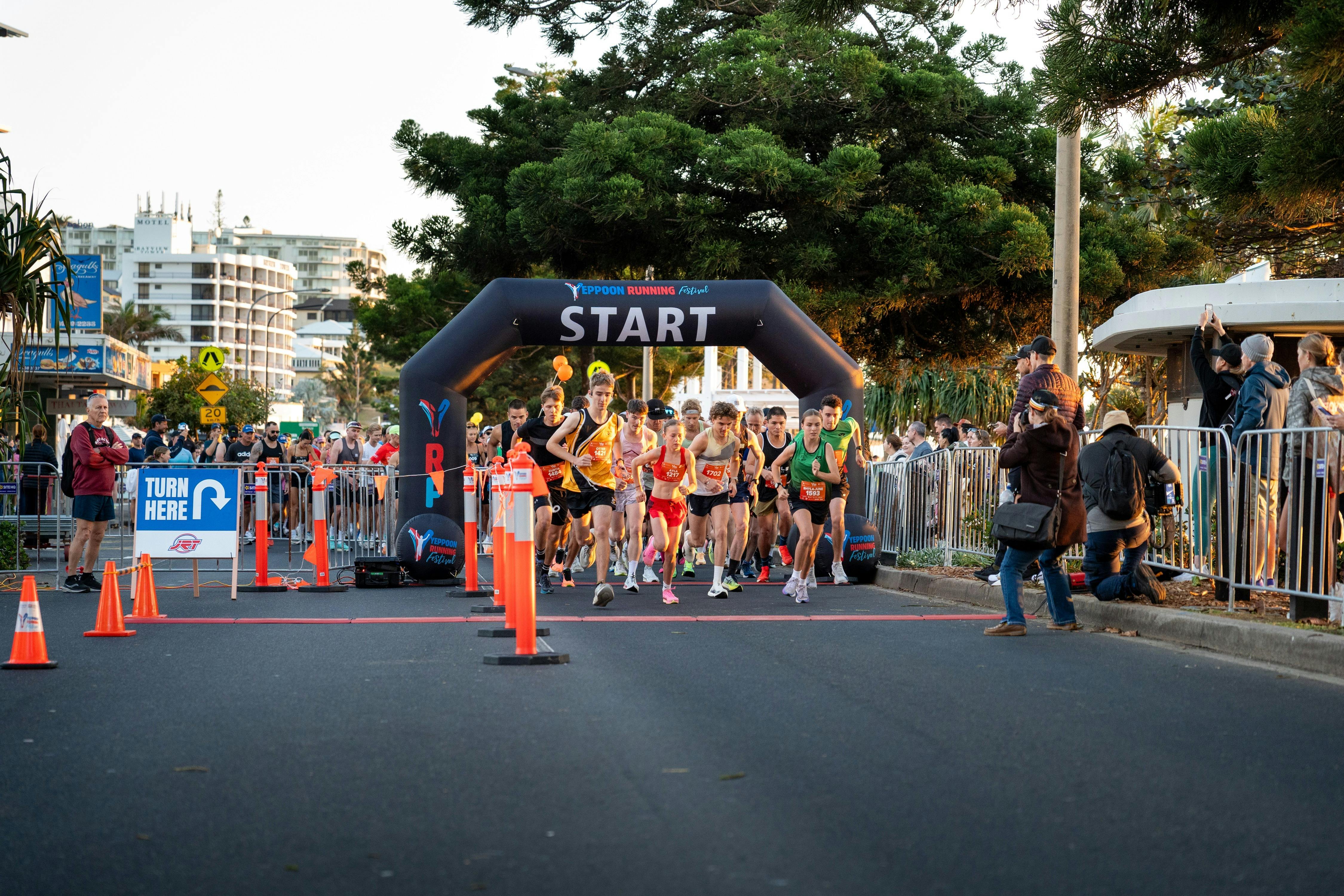A large field of runners crosses the festival start line as spectators watch from both sides of the