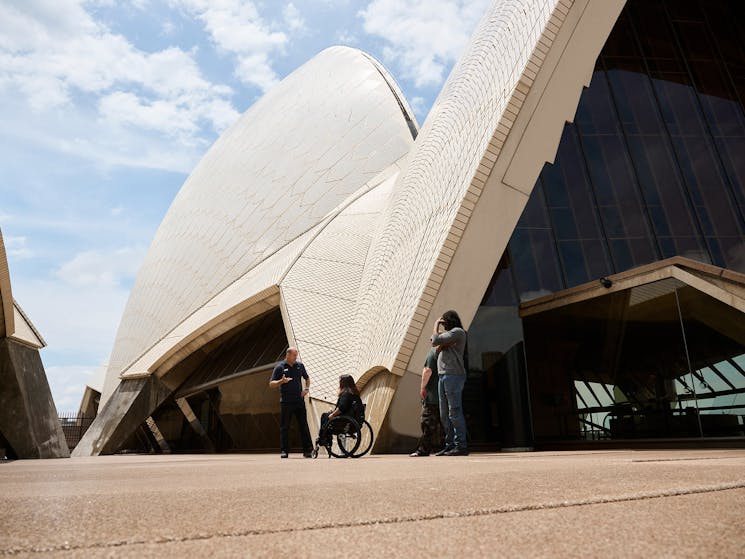 Woman in wheelchair with her family and tour guide looking at the Opera House sails
