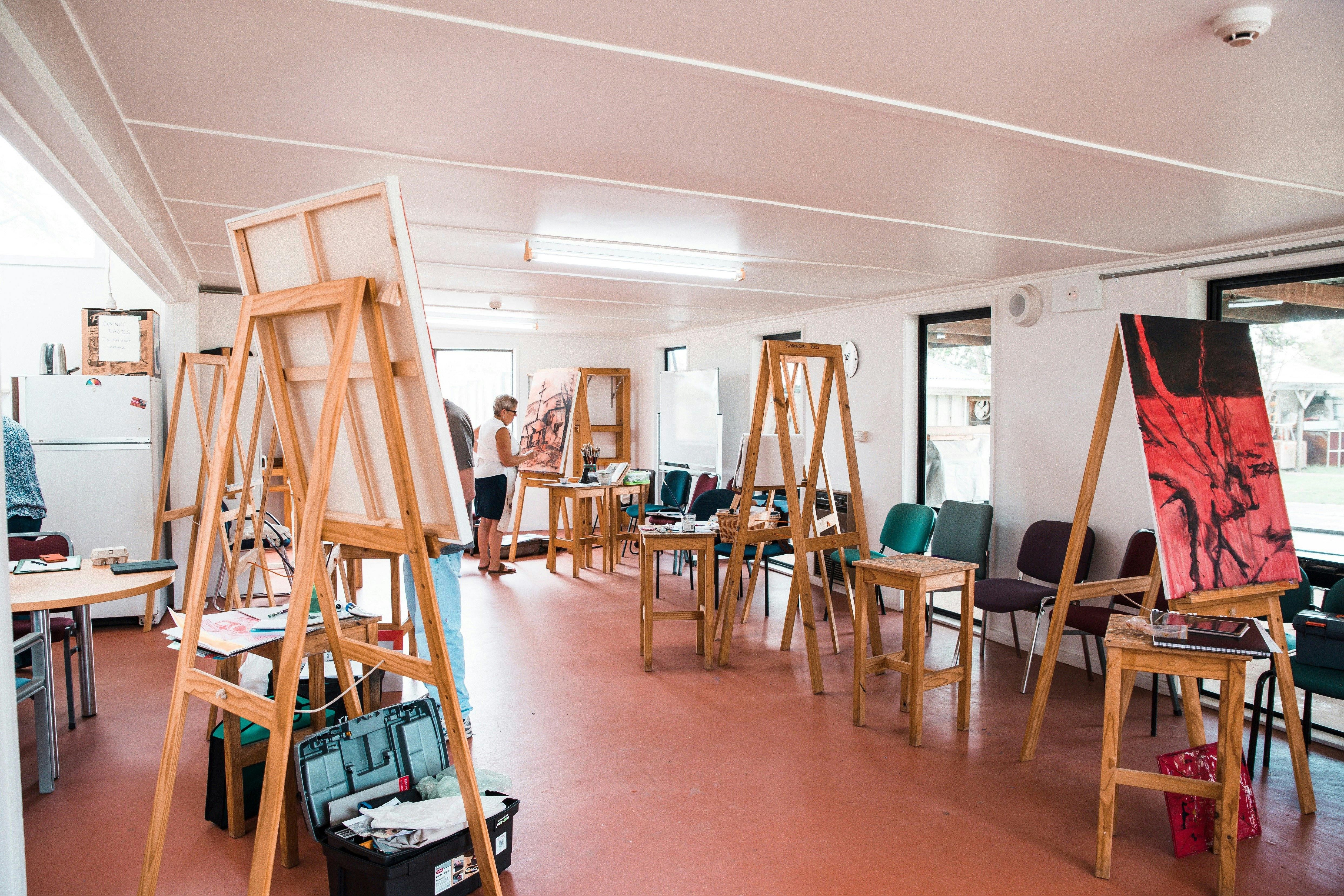 Several easels holding large canvases are set up in a large room.