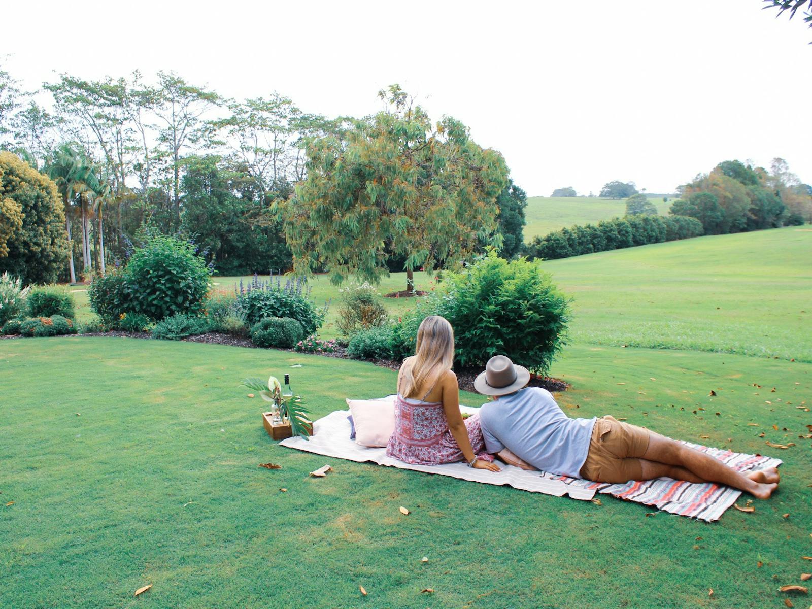 Image of a couple sitting on a picnic rug overlooking the rolling green hills of Summerland Farm