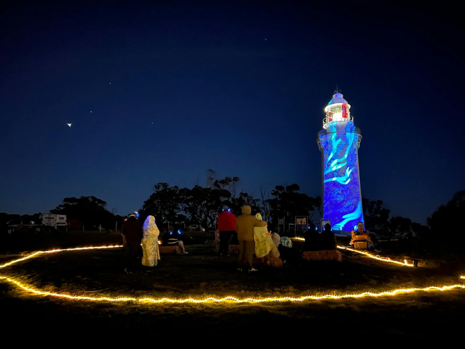 People looking at nighttime projections onto Table Cape lighthouse.