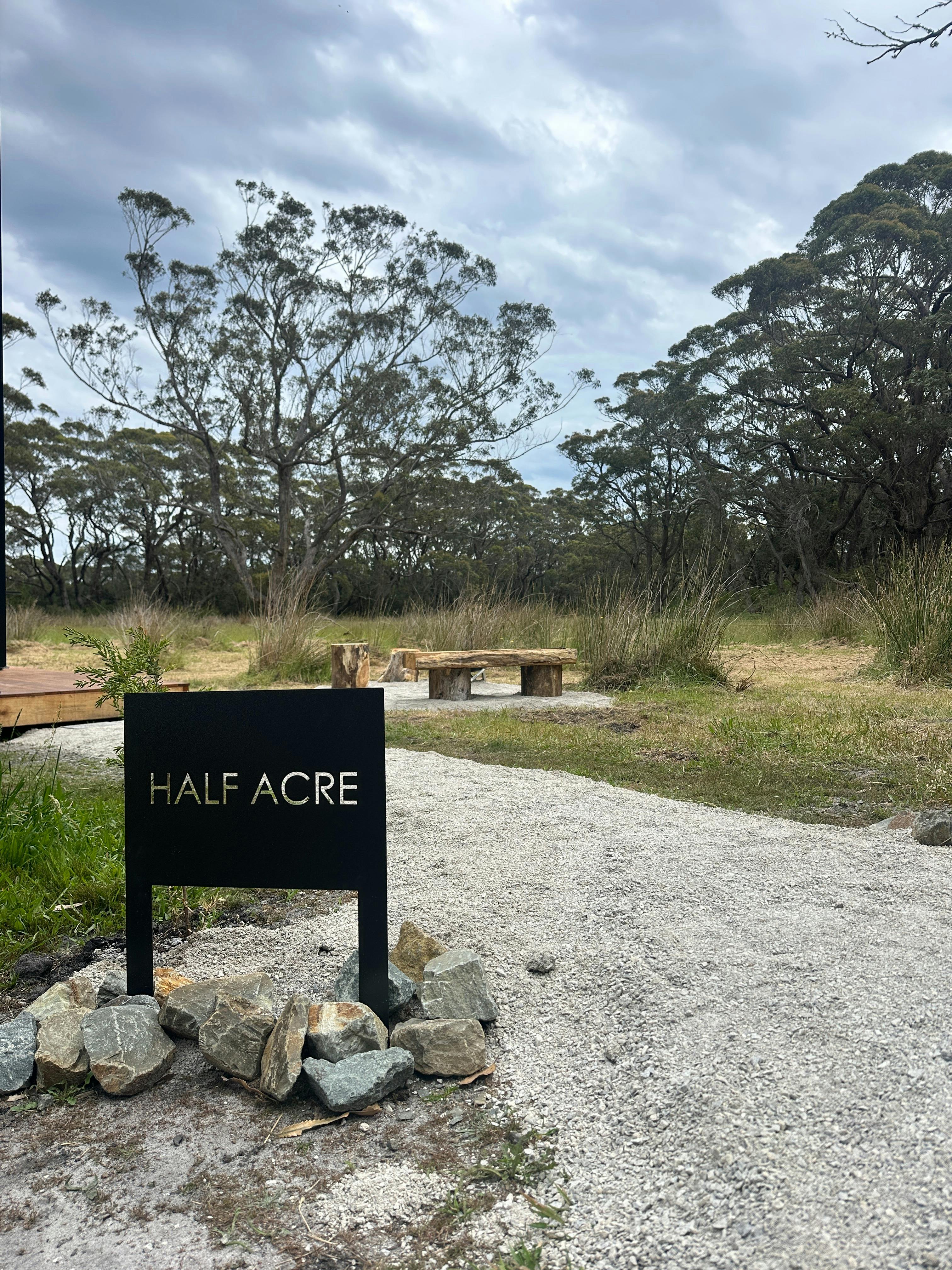 A black sign with 'Half Acre' is placed in front of an outdoor seating area, fire pot & native bush