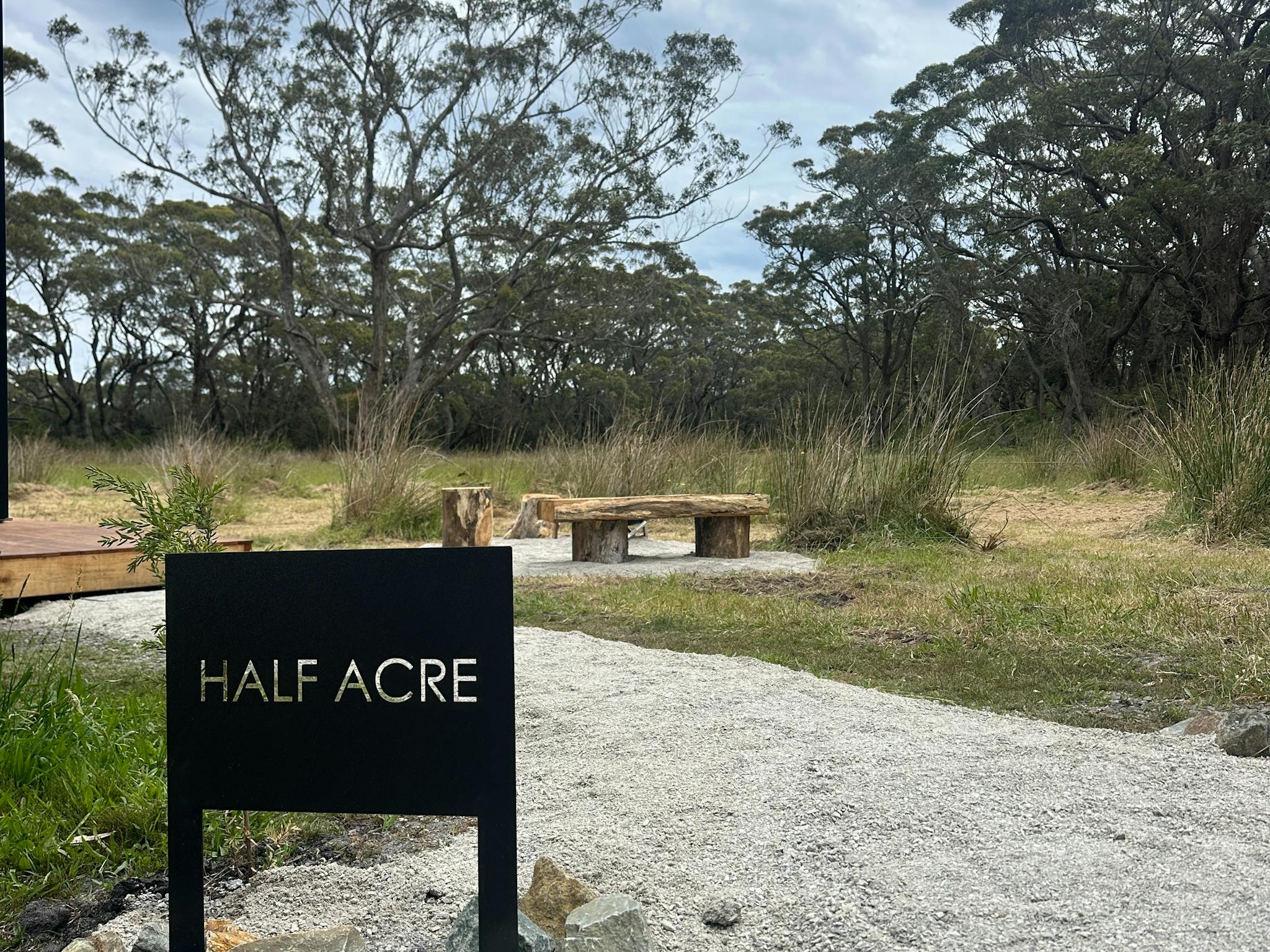 A black sign with 'Half Acre' is placed in front of an outdoor seating area, fire pot & native bush