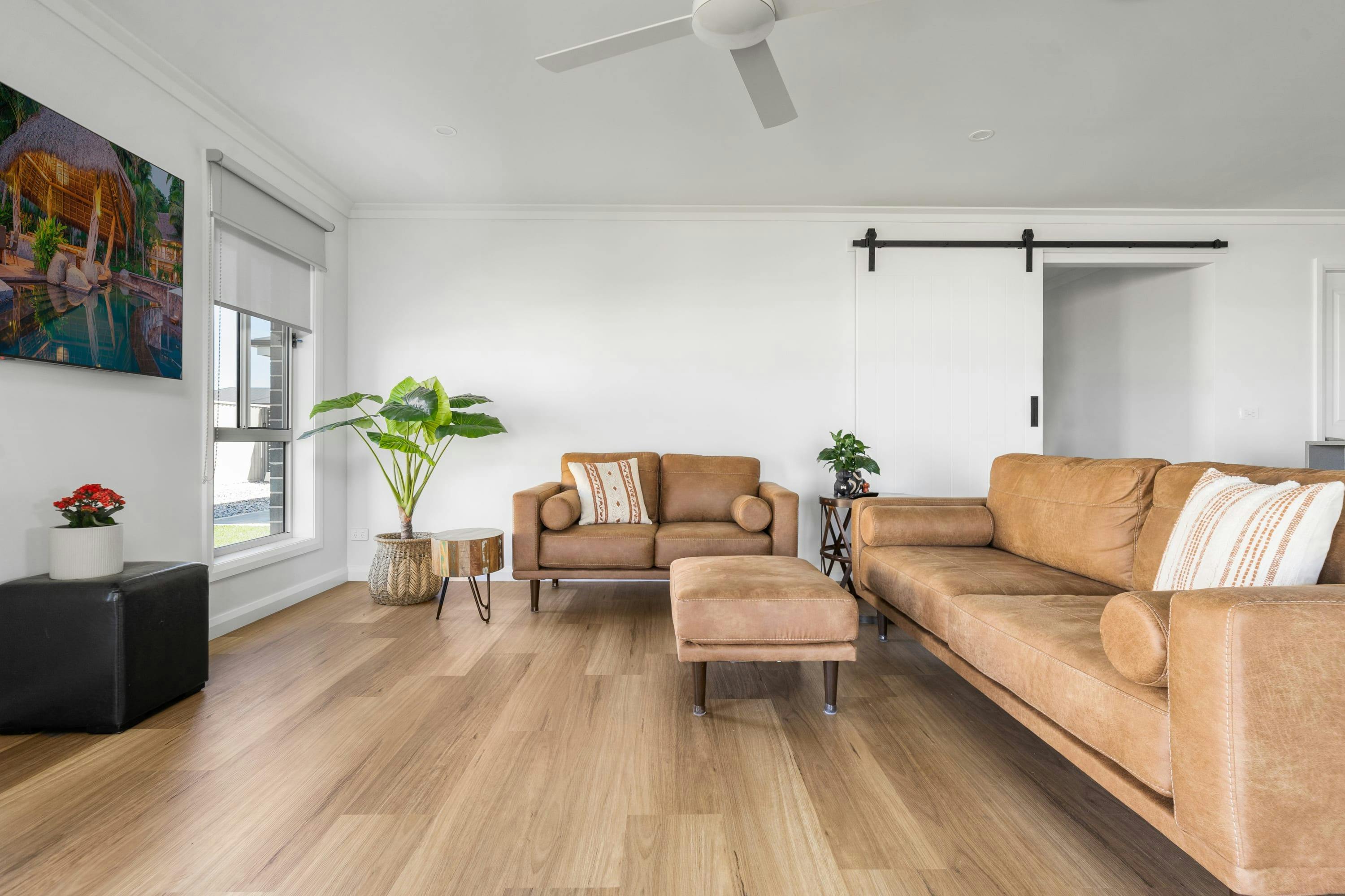 2 brown leather couches with an ottoman, large smart tv mounted to the wall.