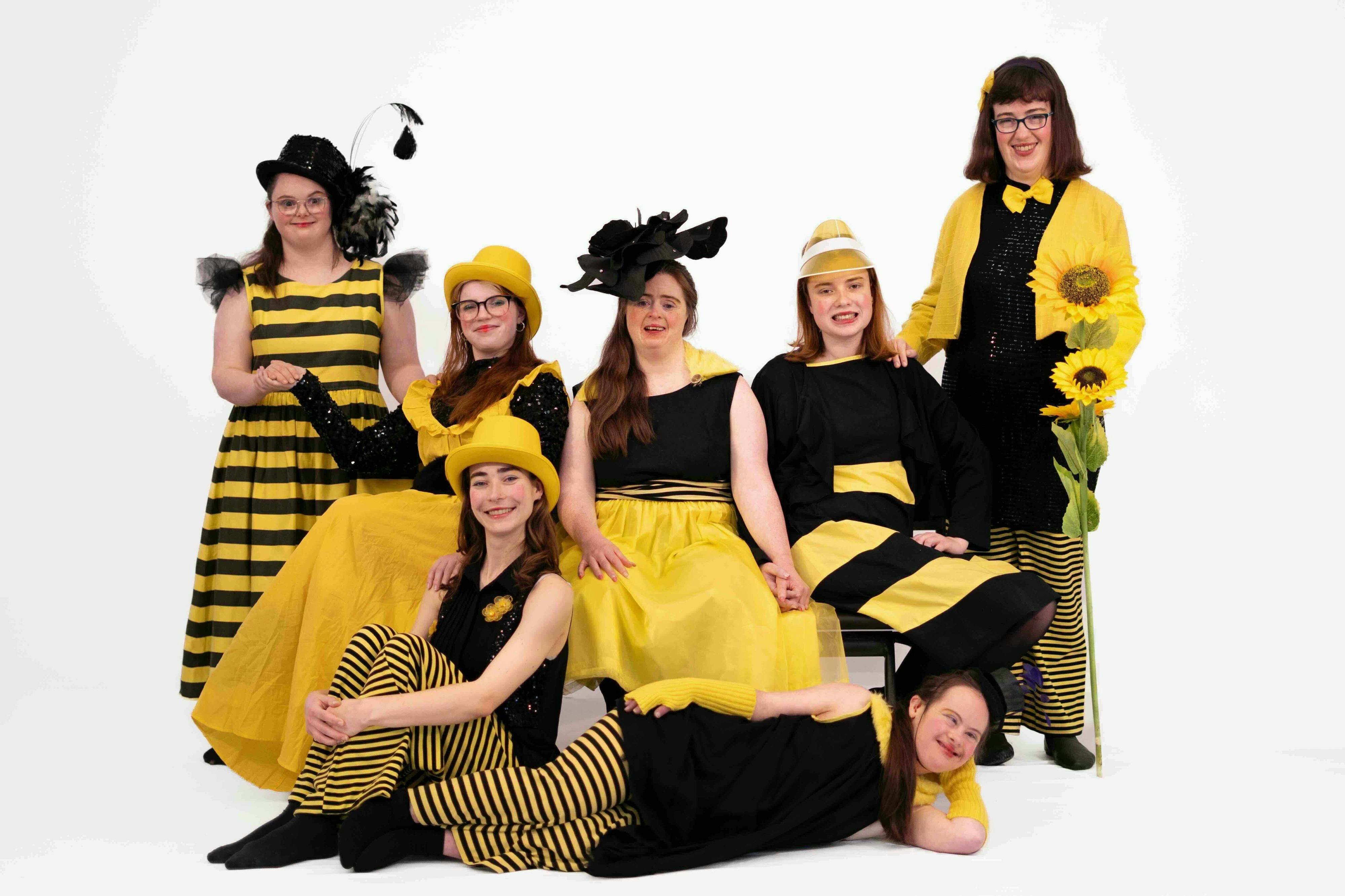 A group of dancers dressed in yellow and black reminiscent of bees pose for a group photograph
