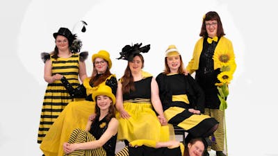 A group of dancers dressed in yellow and black reminiscent of bees pose for a group photograph
