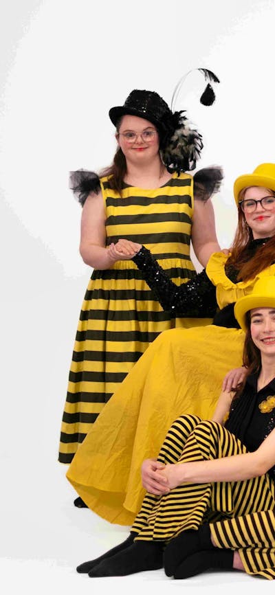 A group of dancers dressed in yellow and black reminiscent of bees pose for a group photograph