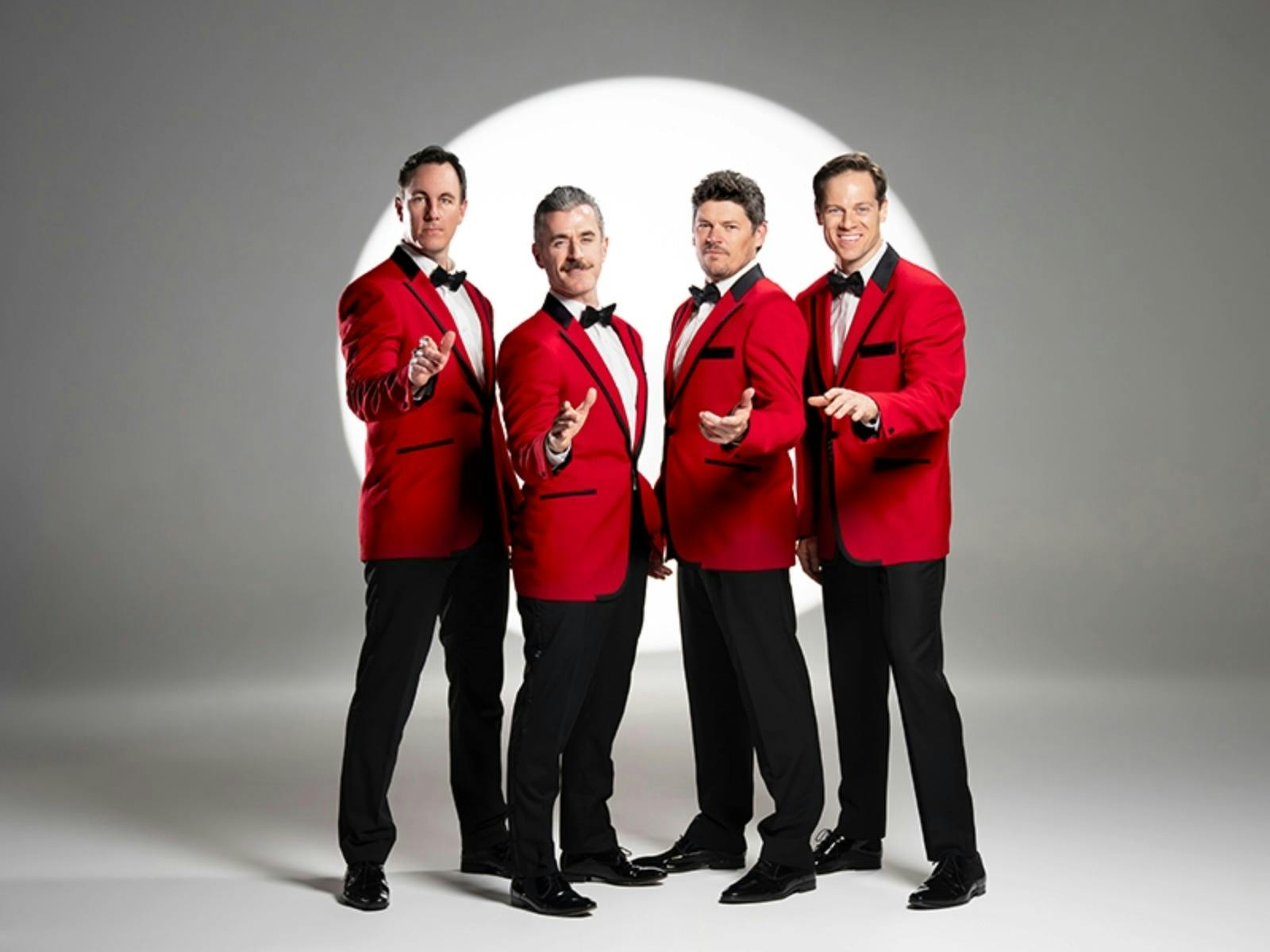 4 men in red jackets and clack pants in front of a spotlight on grey wall
