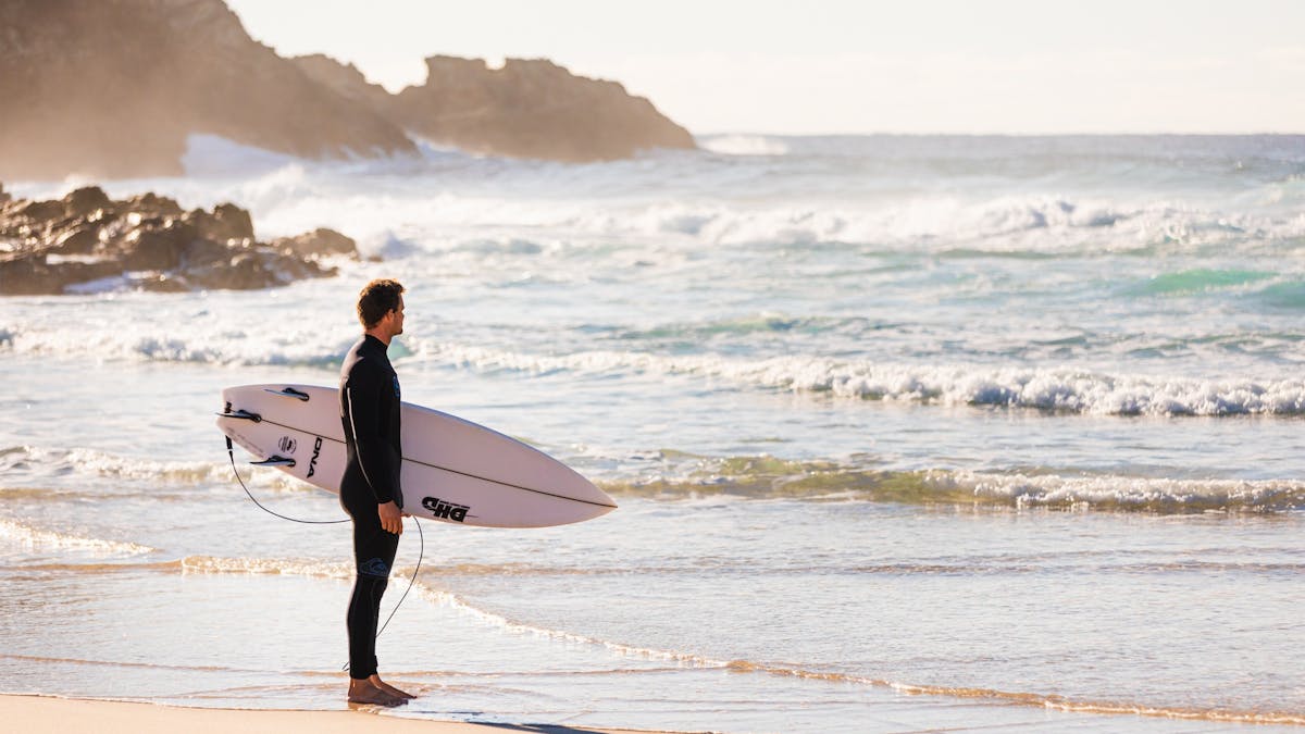 Surfer standing at Main Beach, North Stradbroke Island (Minjerribah), looking out at the ocean waves