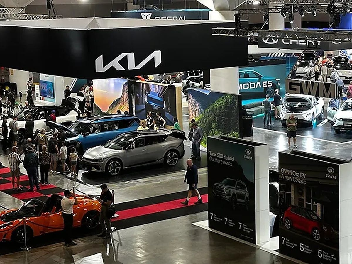 Crowds explore EVs at indoor car show.