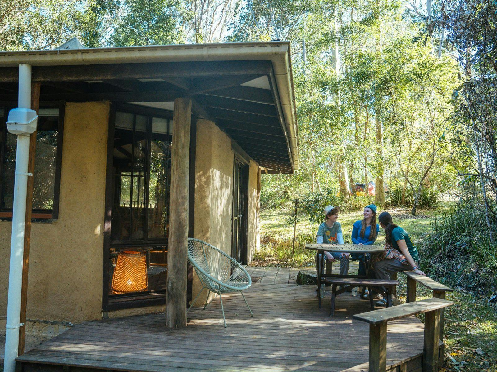 People sit on deck of Melia Cottage at Wangat Lodge, surrounded by forest in the Hunter Valley