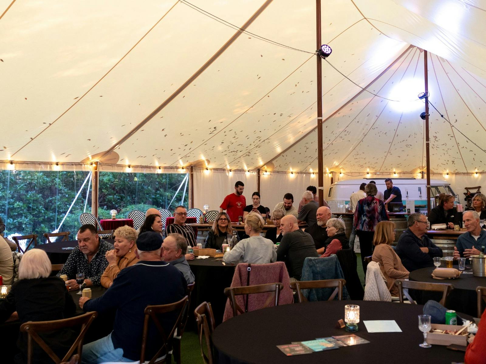 people seated at banquet tables at a daytime event under marquee