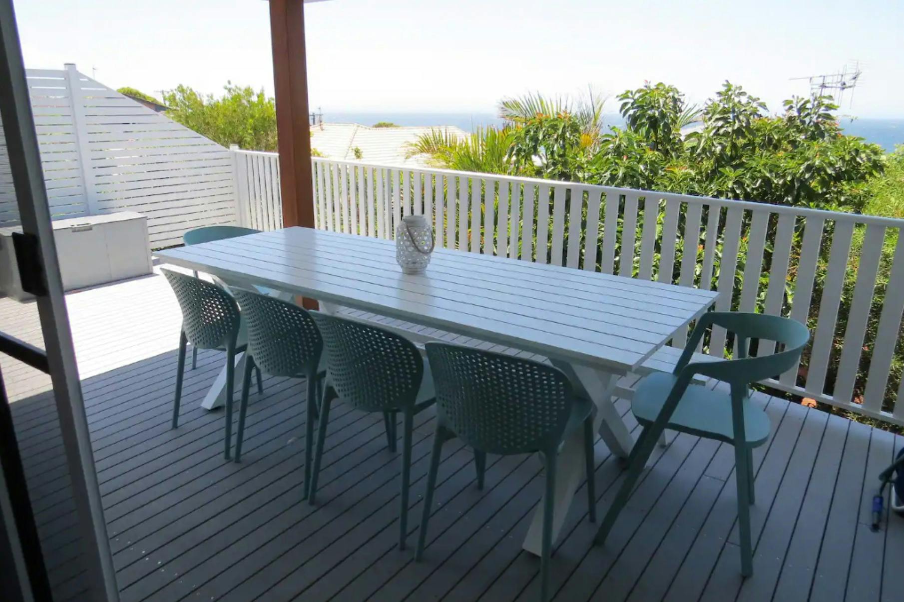 녹지로 둘러싸여 멀리 바다가 보이는 데크의 야외 식사 공간