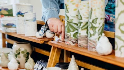 A hand touching some ceramic vessels on a market stall display