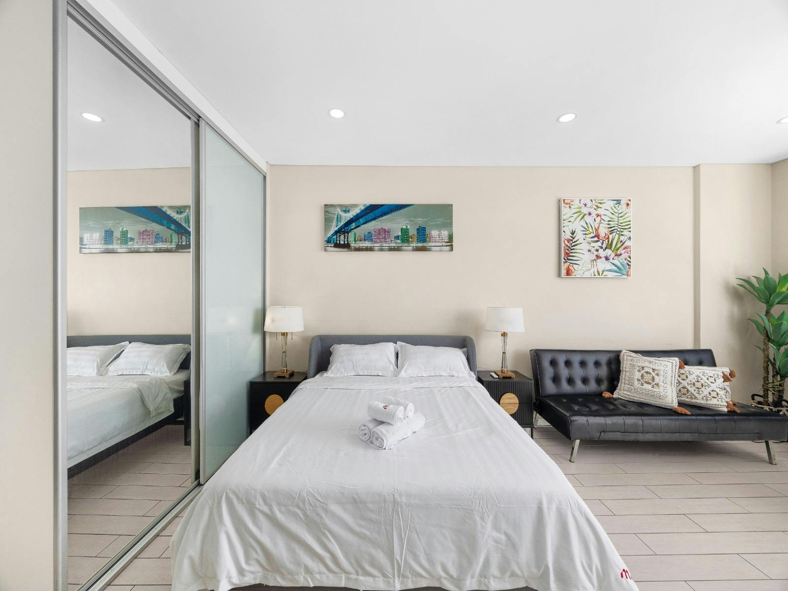 Bedroom featuring a queen-size bed, mirrored wardrobe, bedside tables, and modern artwork.