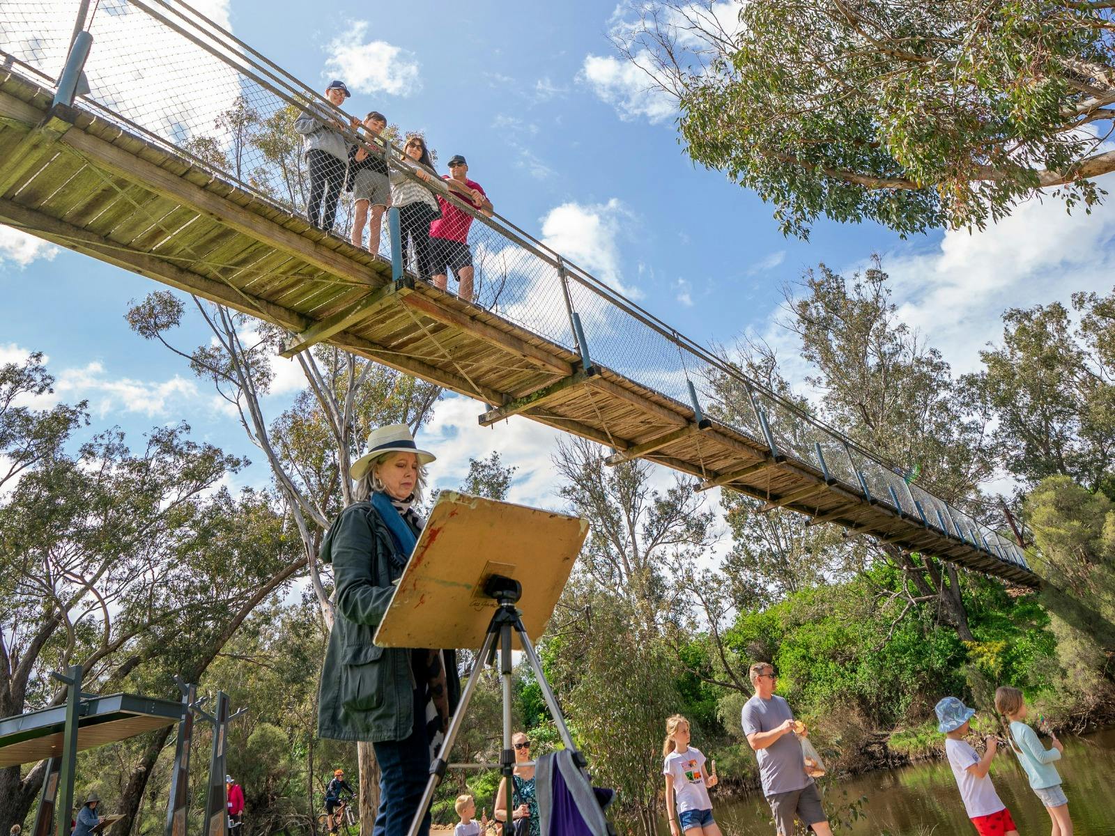 Family of four look down from the Pinjarra Suspension Bridge at an artist painting their surrounds