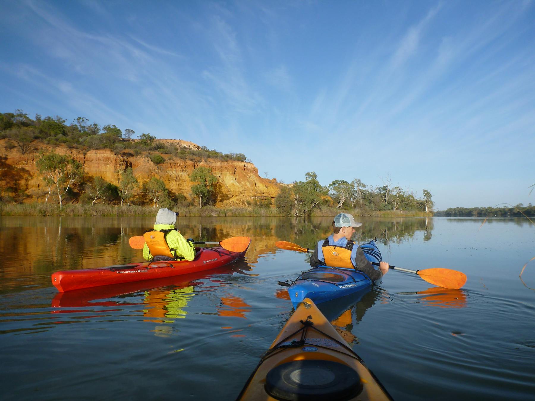 Kayakers on the Murray River in Berri, near cliffs, under a blue sky.