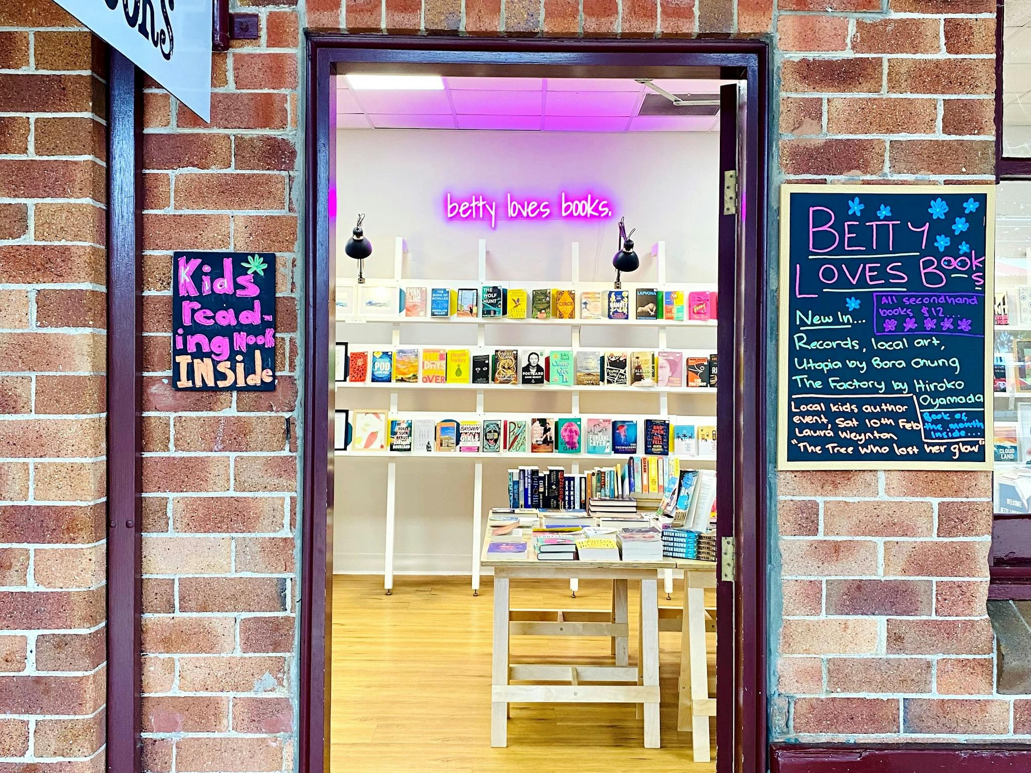 lookiong through a door you see bookshelves covered in colourful books and a neon sign