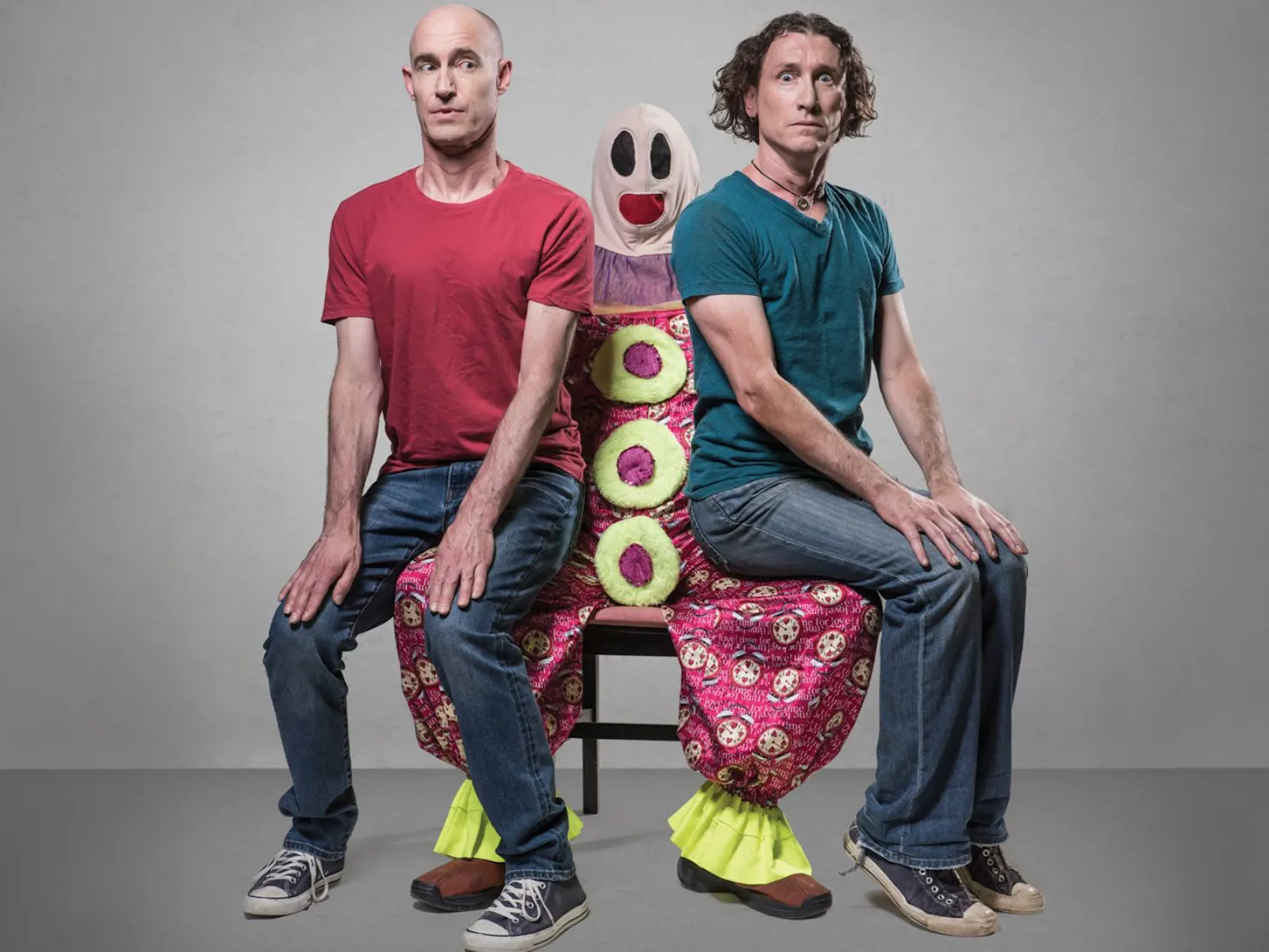 2 men red tshirt on left green on right sitting on a clown