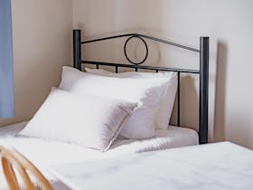 Close-up of a neatly made single bed with white linens and soft pillows.