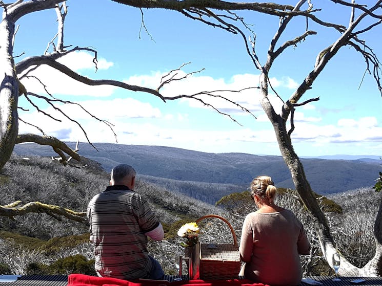 Couple enjoying their picnic and wine as the look over the Bogong High Plains and beyond