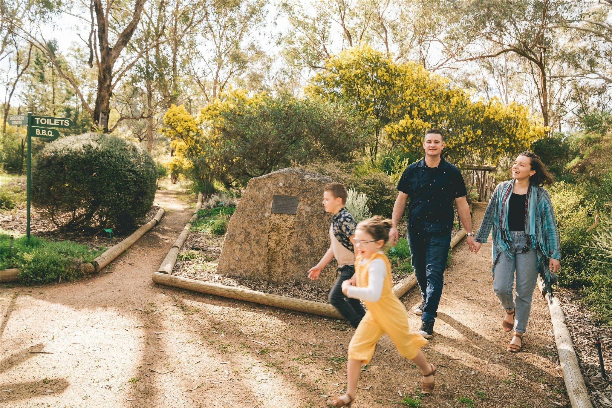 Two children running through the garden with parents walking behind