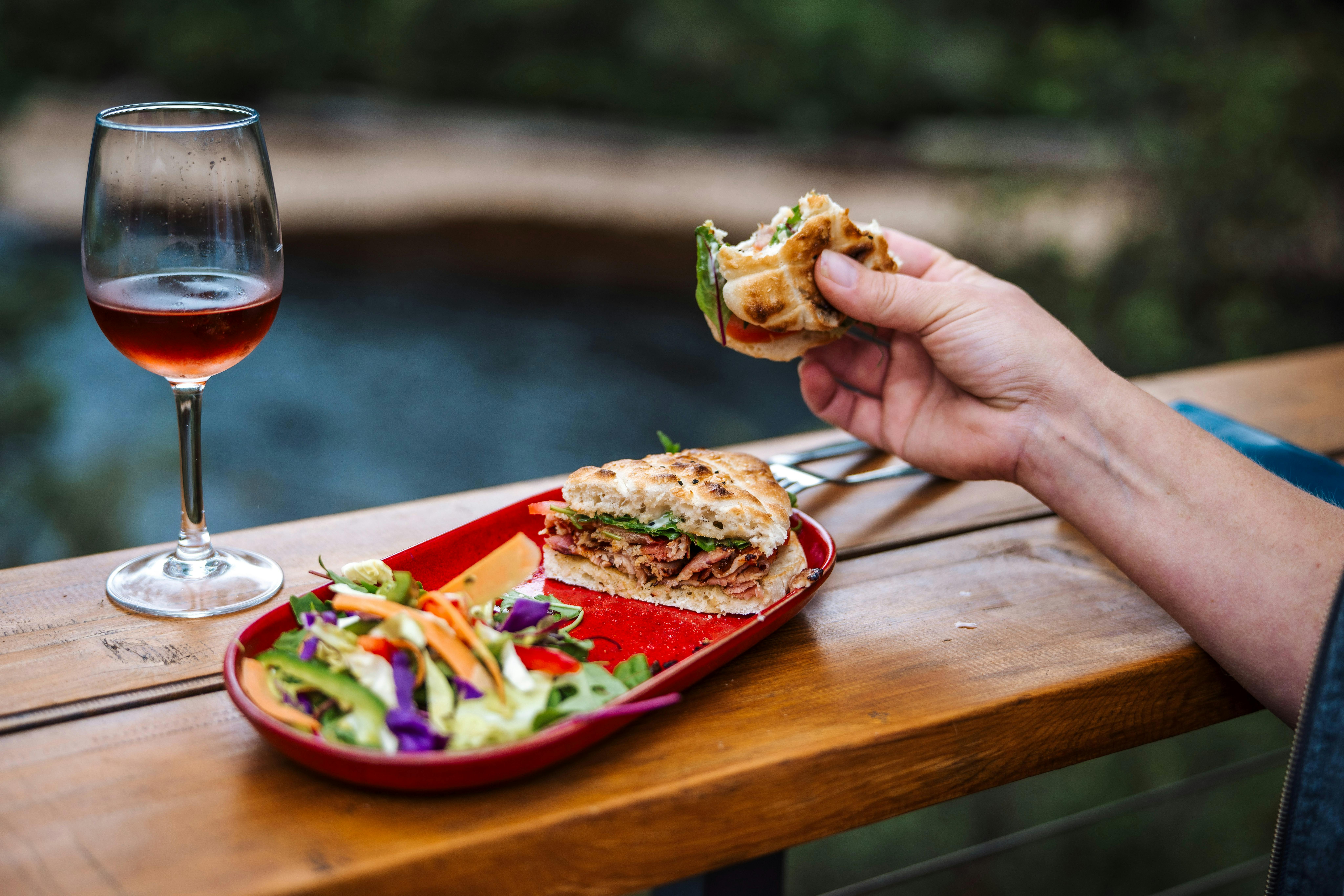 a half eaten BLT sandwich and glass of wine, sitting on a bench that overlooks the rivre
