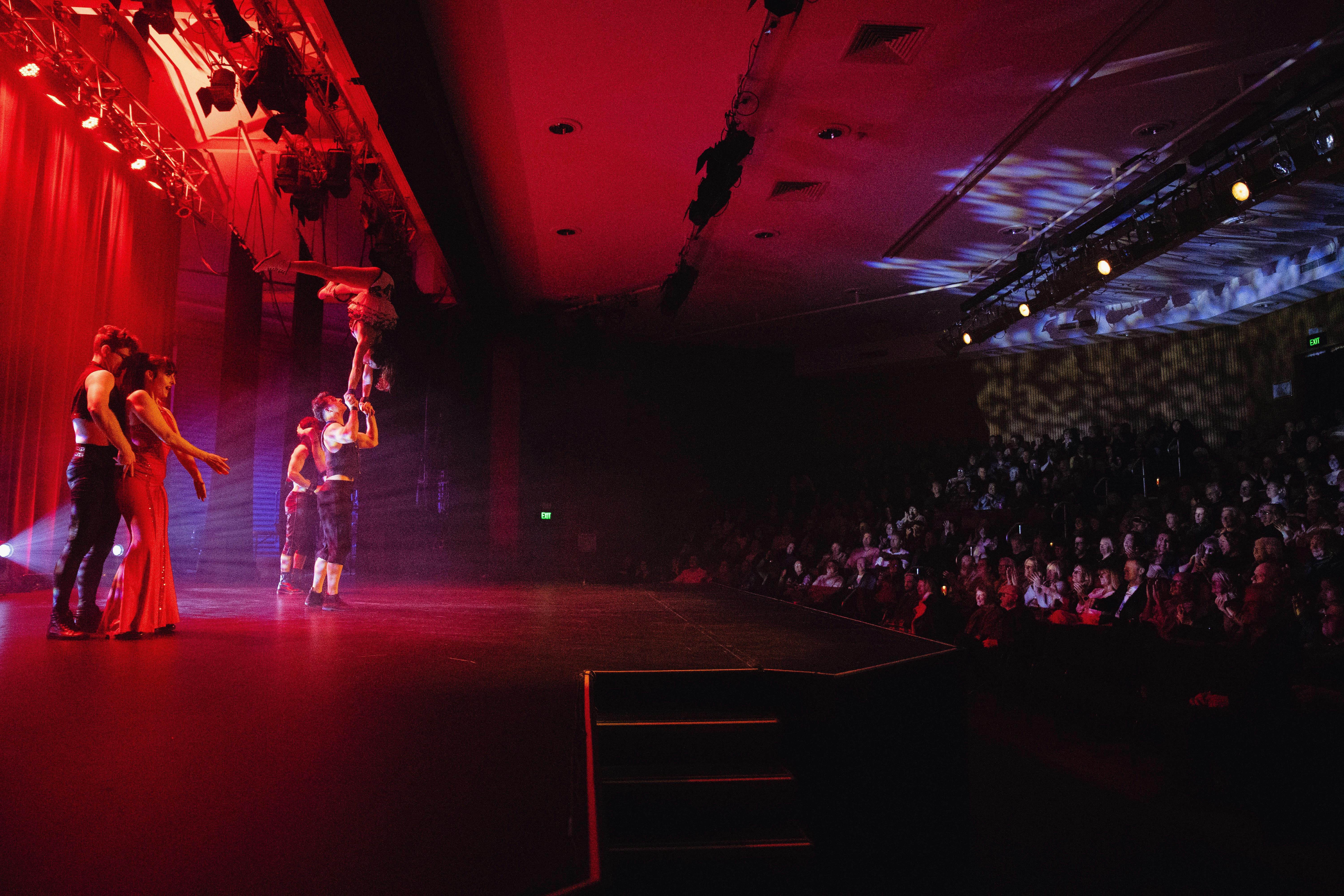 A circus has a person suspended in the air on the Forge Theatre stage. The audience is onlooking.