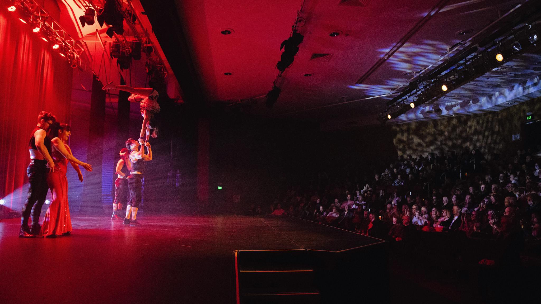 A circus has a person suspended in the air on the Forge Theatre stage. The audience is onlooking.