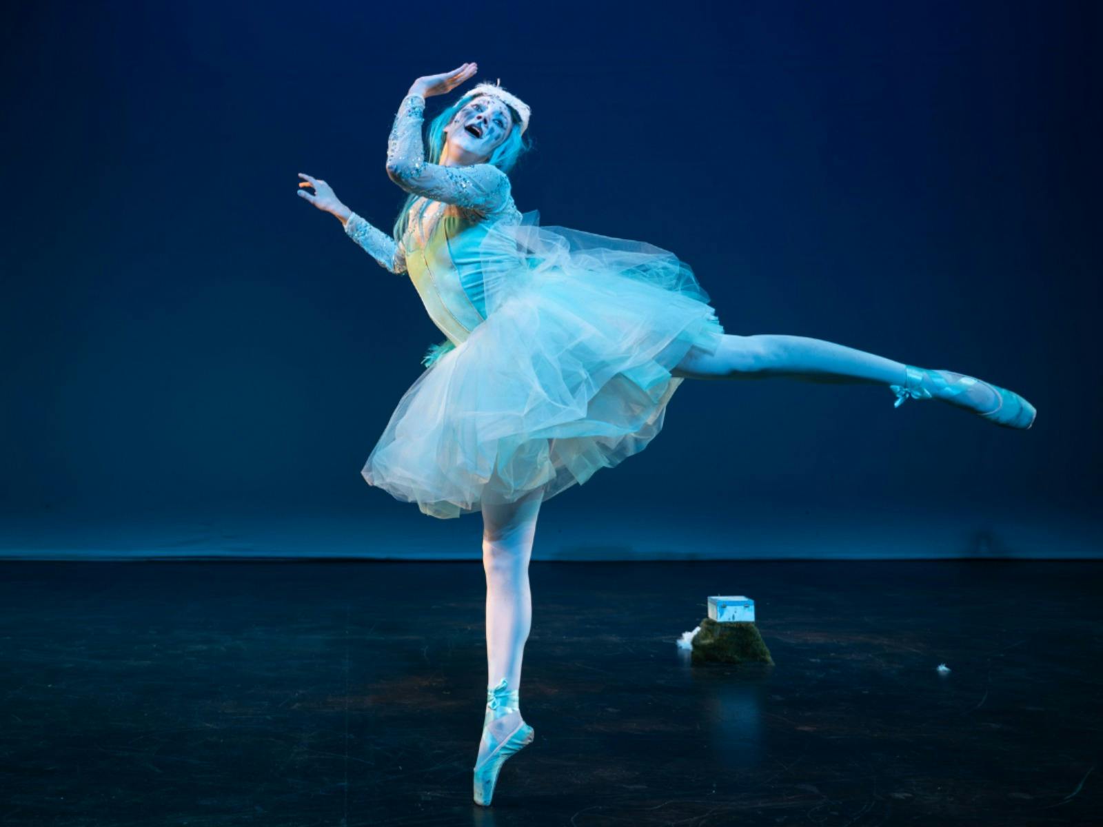 A woman dressed in a blue ballerina outfit striking a pose on a black stage