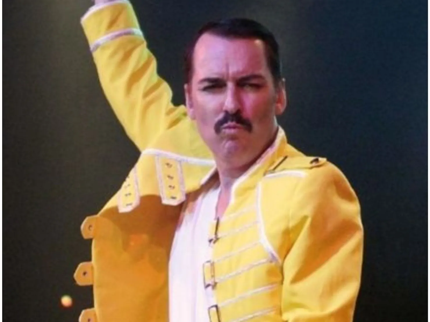 Man with moe in yellow jacket with arm raised