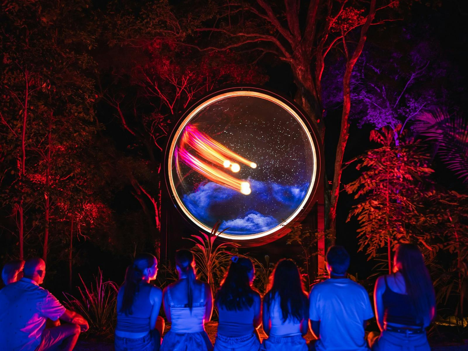 Group of people sitting on bench watching a colourful light spectacle inside a round circle. Group of people sitting on bench watching a colourful light spectacle inside a round circle.