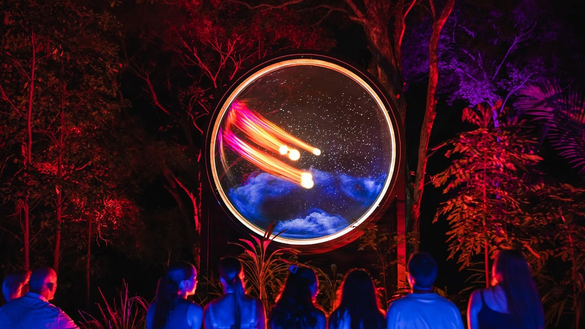 Group of people sitting on bench watching a colourful light spectacle inside a round circle.