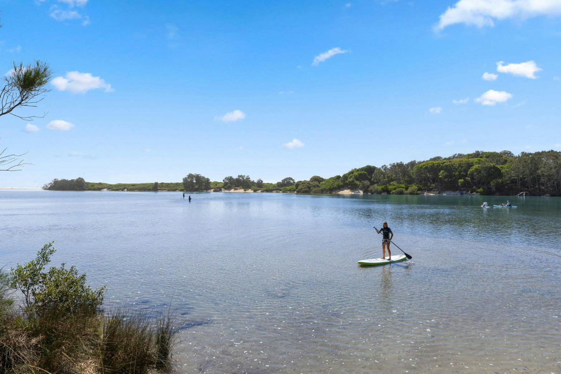 맑고 푸른 강 이미지. 배경에서는 남자들이 낚시를 하고 있고 전경에서는 여자 한 명이 SUP를 타고 있습니다.