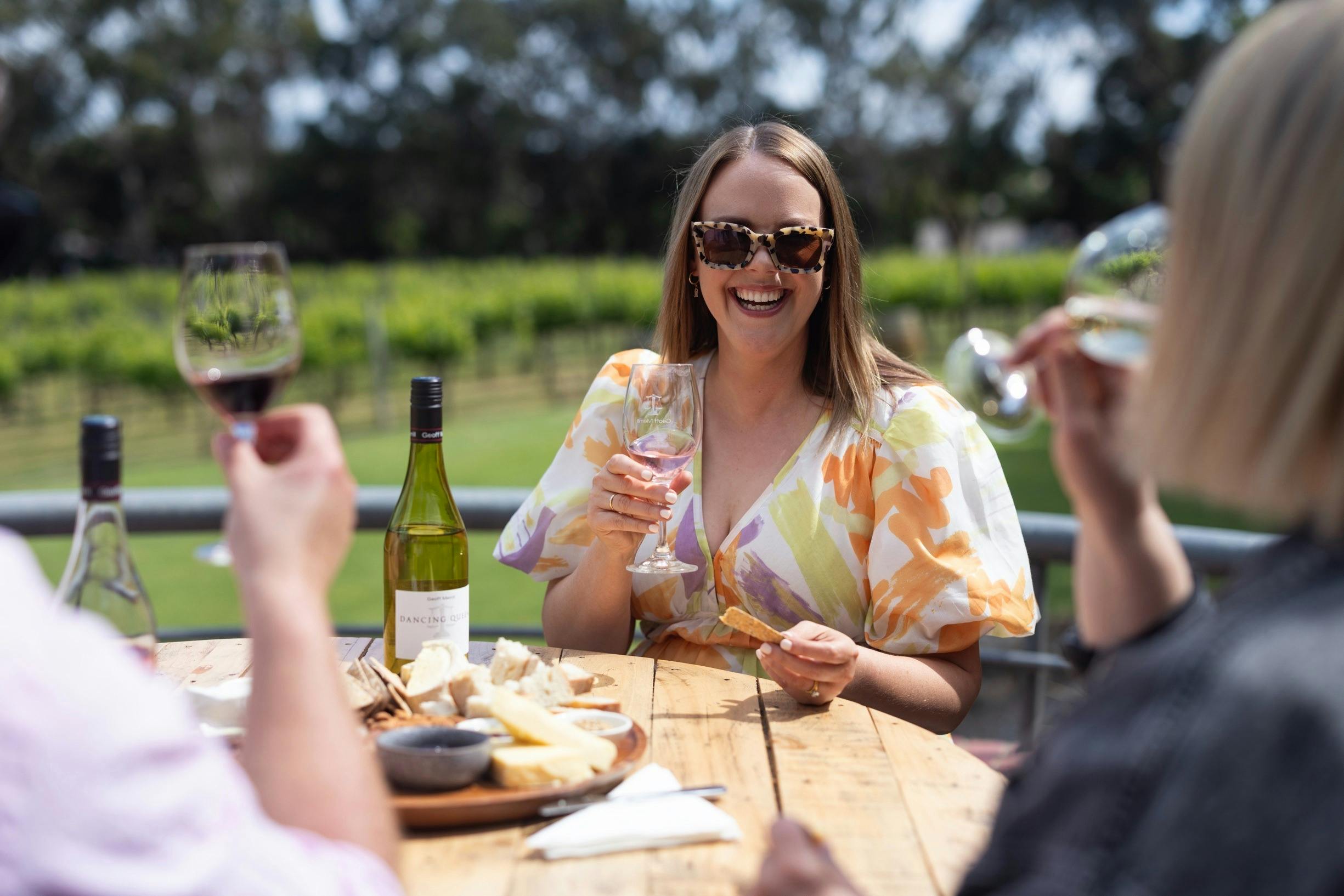 A woman with sunglasses holding a wine and smiling