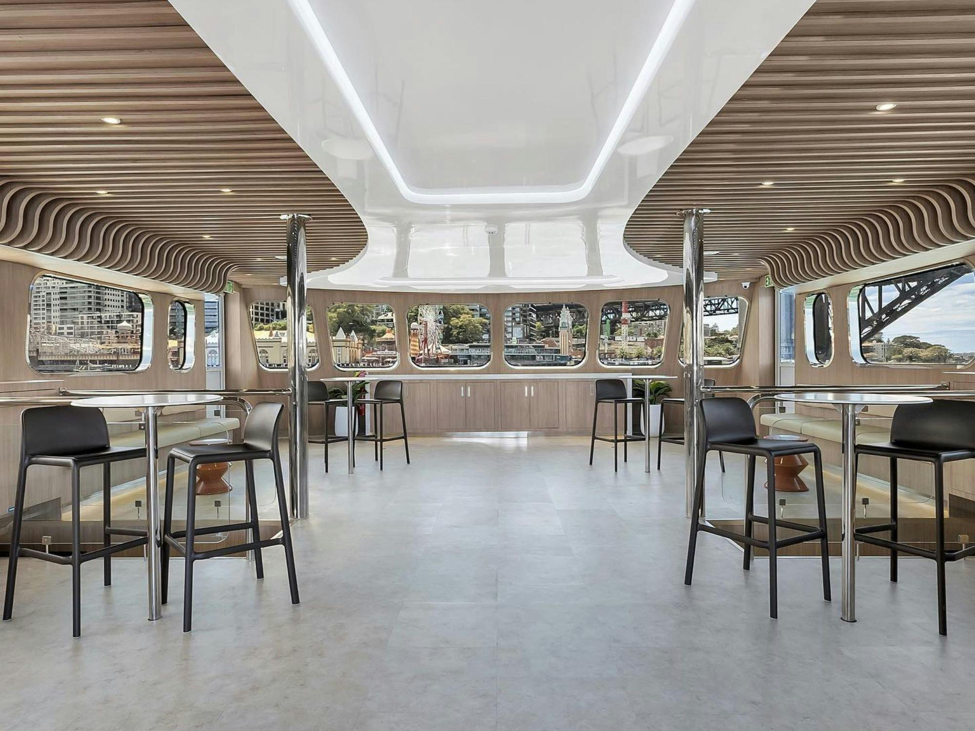 Indoor lounge area on Karisma 2 with bar stools, tables and Sydney harbour views through windows