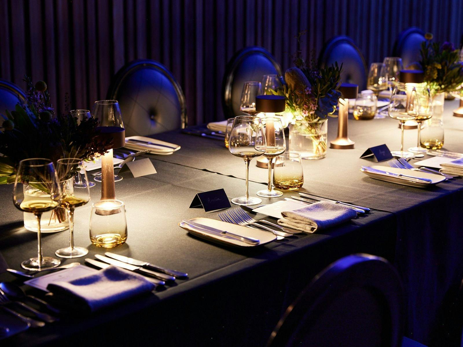 Table set with plates, cutlery, wine glasses and table lights on a black tablecloth
