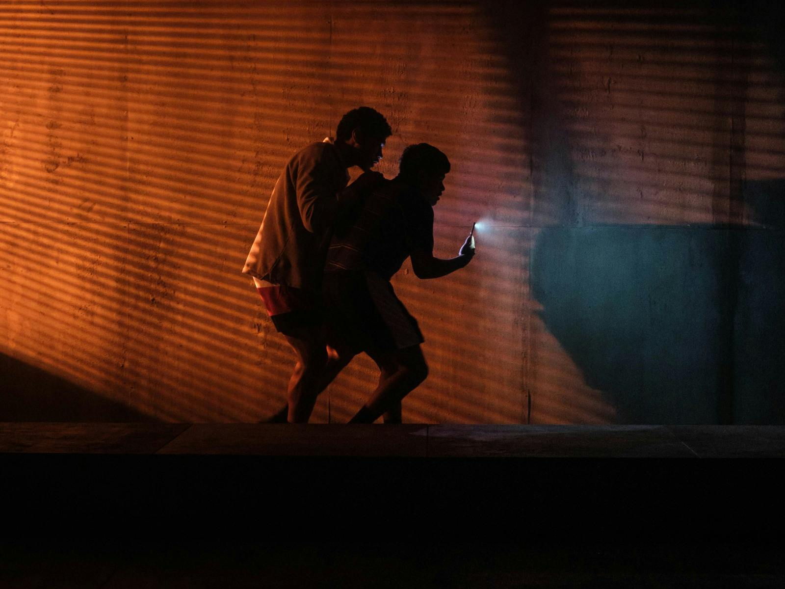 Two young people walking down a dark corridor with their phone flashlight on