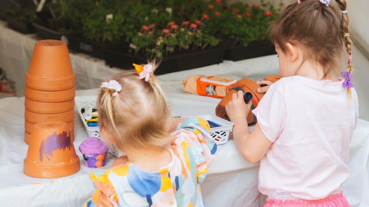 Two young girls paint terracotta pots. The face away from the camera.