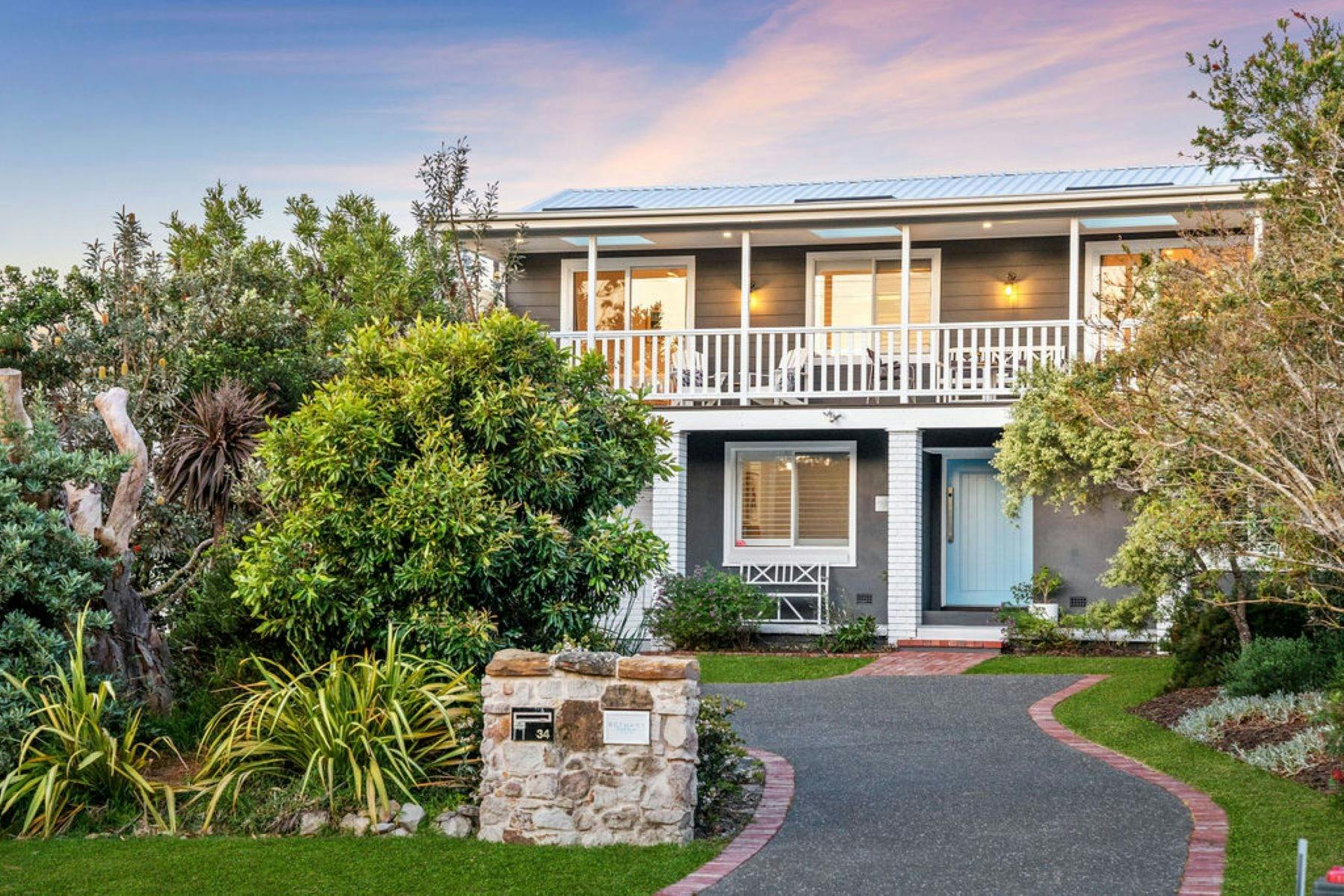 정면 외관 이미지. 태양이 앞 창문에 들보를 드리우고 있습니다. 무성한 푸른 나무가 집을 둘러싸고 있습니다.