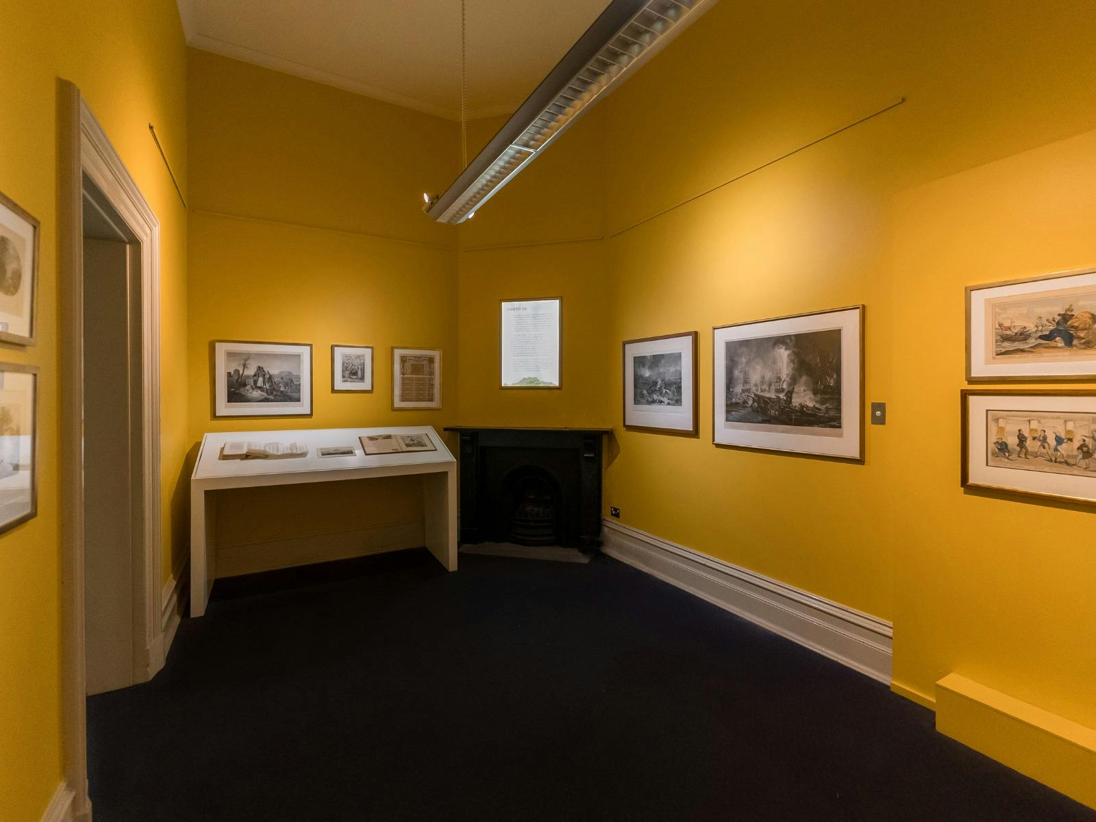 Various artworks hang on walls and a large white plinth in a yellow gallery space
