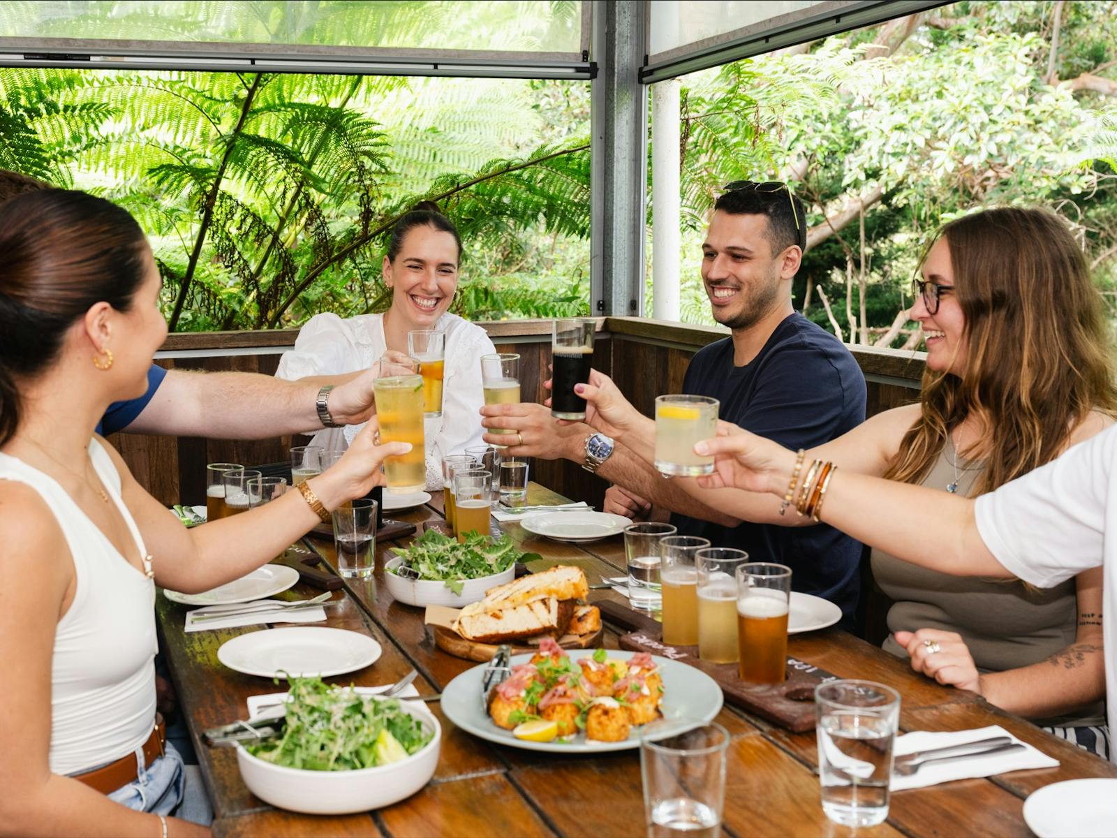 Group of friends cheers'ing drinks over spread of local food